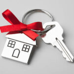 House keys with house shaped keychain with red ribbon on light grey background